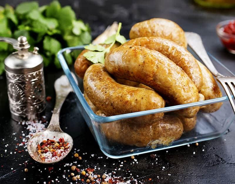 Juicy cooked sausages in a glass dish with spices and herbs.