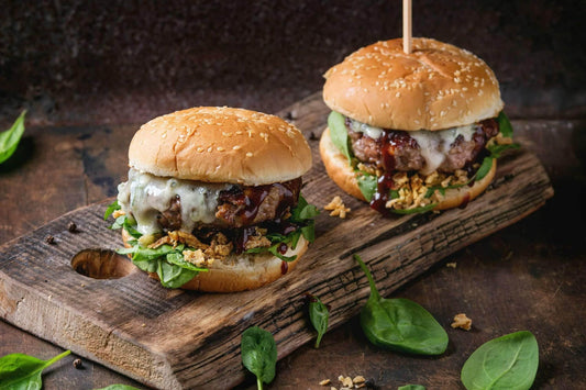 Two gourmet cheeseburgers with spinach, onions, and BBQ sauce.